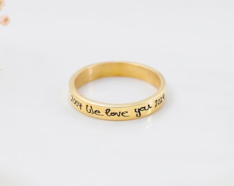 Puede incluir: Un anillo de banda en tono dorado pulido con una superficie exterior lisa y redondeada. El anillo está grabado con el texto negro "2004 We love you 2024" escrito en un estilo cursivo y manuscrito a lo largo de la circunferencia exterior.