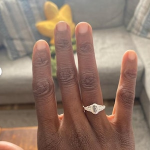 A silver signet ring with a raised letter 'F' in the center. The ring is set with small, clear stones around the letter.