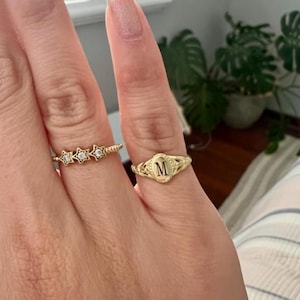 A gold ring with an oval-shaped setting featuring the letter 'M' in black lettering.