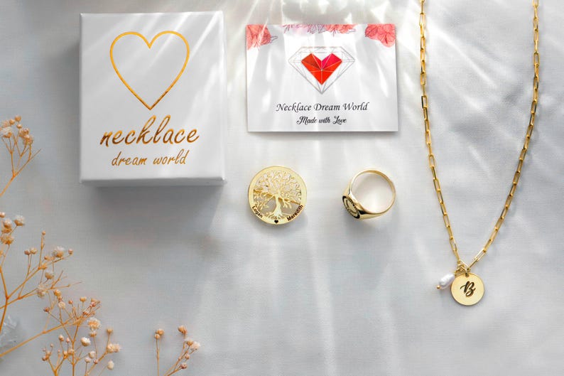 May include: A white gift box with a gold heart and the text necklace dream world, a card with a red heart logo and text, a gold tree of life circular pendant, a gold signet ring, and a gold chain necklace with a letter B pendant and a small pearl.