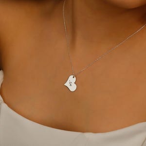 A silver heart-shaped pendant necklace with the word 'Geo' engraved on it.