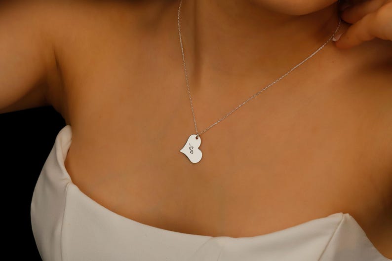 A silver heart-shaped pendant necklace with the word 'Geo' engraved on it.