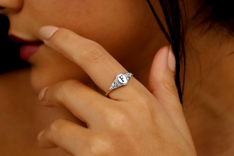 A silver signet ring with a white oval shaped stone featuring the letter 'F' in black.