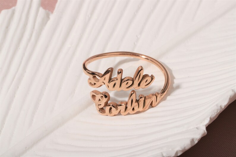 A rose gold-toned ring with the names 'Adele' and 'Corbin' engraved on it.