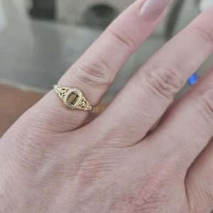 A gold ring with an oval-shaped setting featuring the letter 'L' in black lettering.