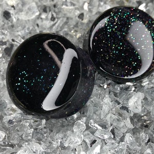 May include: Pair of black glass ear gauges with iridescent glitter embedded in the glass.