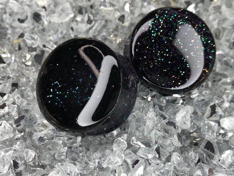 May include: Pair of black glass ear gauges with iridescent glitter embedded in the glass.