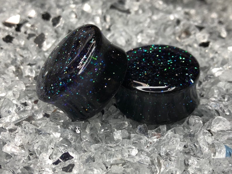 May include: Pair of black ear gauges with iridescent glitter embedded in the resin.