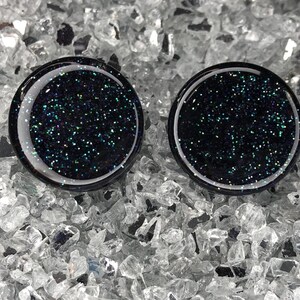 May include: Two black round glass cabochons with iridescent glitter embedded in the glass.