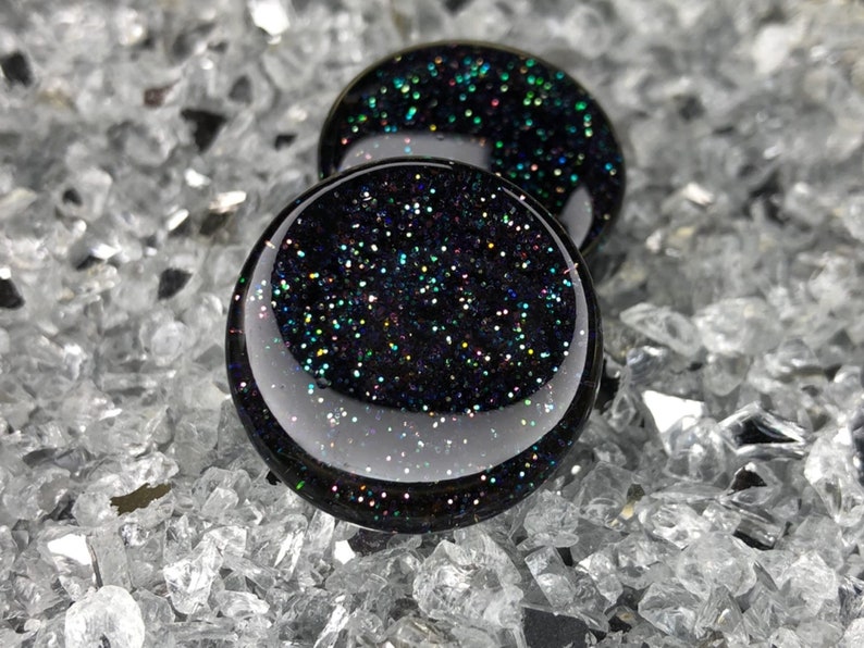 May include: Two black glass round plugs with iridescent glitter embedded in the glass.