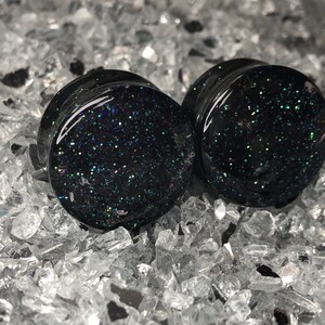 May include: Pair of black ear gauges with iridescent glitter embedded in the resin.