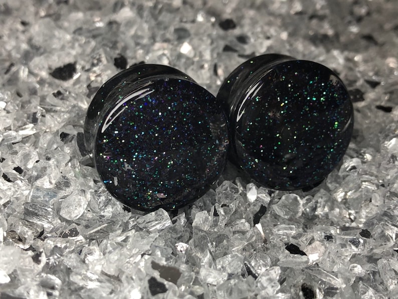 May include: Pair of black ear gauges with iridescent glitter embedded in the resin.