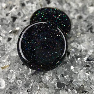 May include: Two black glass ear gauges with iridescent glitter embedded in the glass.