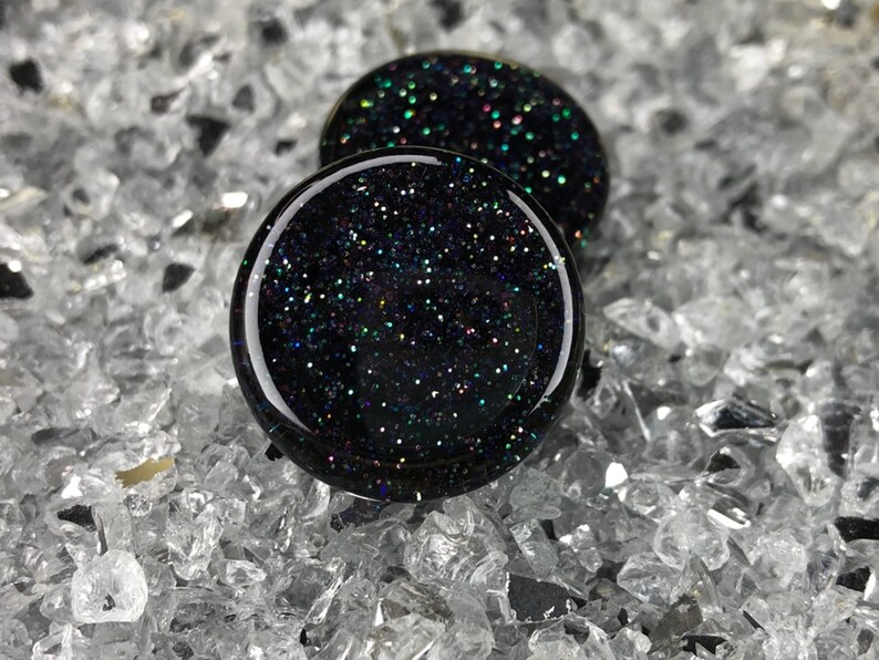 May include: Two black glass ear gauges with iridescent glitter embedded in the glass.