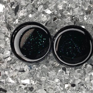 May include: Pair of black ear gauges with embedded green glitter.