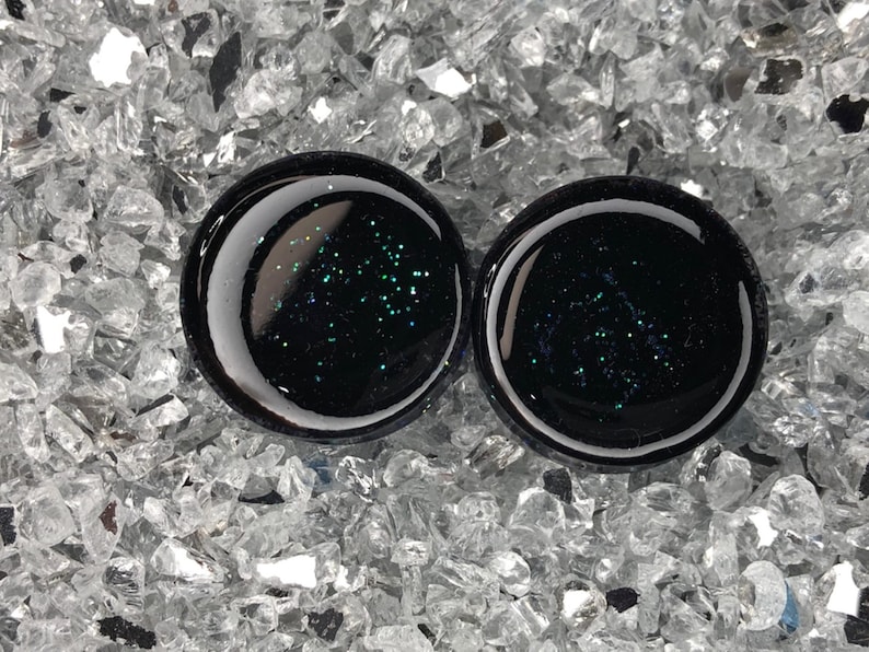 May include: Pair of black ear gauges with embedded green glitter.
