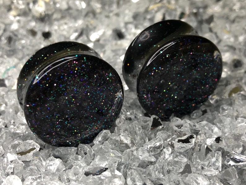 May include: Pair of black ear gauges with iridescent glitter embedded in the resin.