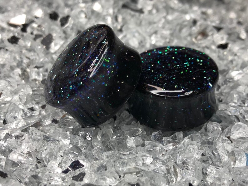 May include: Two black ear gauges with iridescent glitter embedded in the resin. The gauges are round and have a smooth, polished finish.
