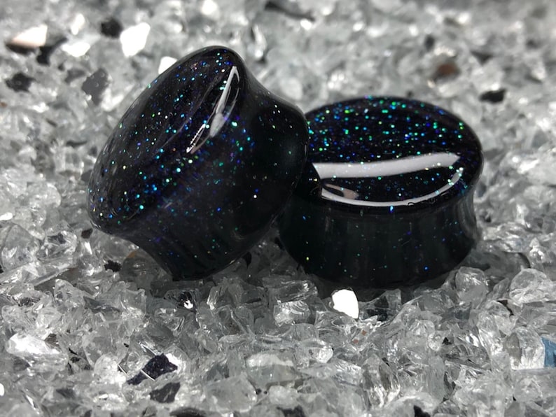 May include: Pair of black ear gauges with embedded iridescent glitter.