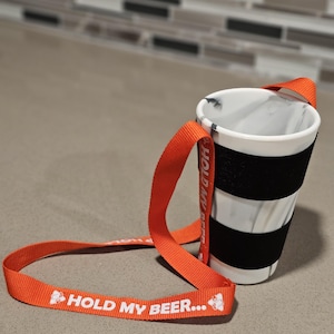 May include: Orange and white "Hold My Beer..."  strap with a black and white striped cup holder.