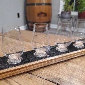 Könnte beinhalten: Ein Tablett aus Holz mit einer schwarzen Oberfläche hält vier klare Whisky-Probiergläser aus Glas. Das Tablett ist aus recyceltem Holz gefertigt und hat eine natürliche Holzoptik.