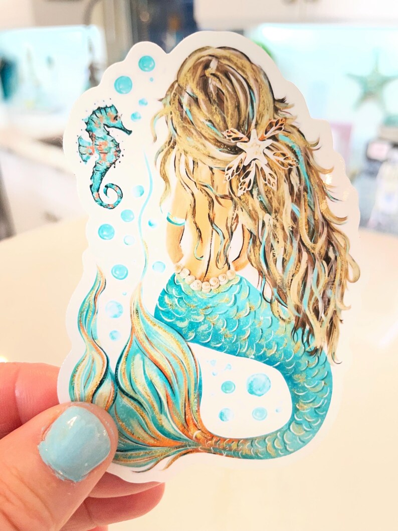 Peut inclure: Autocollant de sir&egrave;ne avec de longs cheveux blonds, une queue turquoise et un collier de perles. Un hippocampe et des bulles sont &eacute;galement repr&eacute;sent&eacute;s. L'autocollant est tenu par une main avec du vernis &agrave; ongles bleu clair.