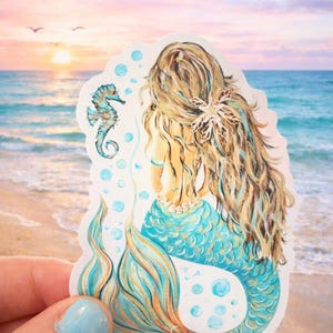 Peut inclure: Un autocollant repr&eacute;sentant une sir&egrave;ne aux longs cheveux blonds et &agrave; la queue turquoise, vue de dos. Un hippocampe et des bulles sont &eacute;galement repr&eacute;sent&eacute;s. L'arri&egrave;re-plan est une sc&egrave;ne de plage avec un coucher de soleil.
