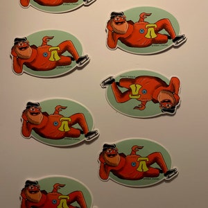 May include: Six red and yellow stickers featuring a cartoon character wearing a red suit and a black hat. The character is lying on their back with their legs in the air. The stickers are on a white background. The text on the stickers reads "@Mikel_Curran".