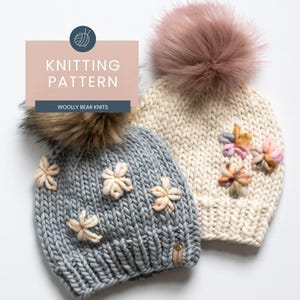 May include: Two knitted beanies with faux fur pom-poms and floral embellishments. One is light gray with beige flowers, the other is cream with colorful flowers. The image includes text that reads "Knitting Pattern" and "Woolly Bear Knits."