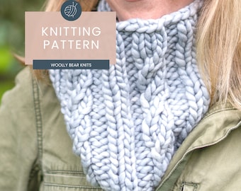 Può includere: Un primo piano di una sciarpa a collo alto di colore grigio chiaro. La sciarpa è realizzata con un filato spesso e presenta un motivo a treccia. Il testo "Knitting Pattern" e "Woolly Bear Knits" è visibile nell'immagine.