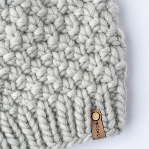 May include: A gray knitted beanie with a brown leather tag that says "WOOLLEY".