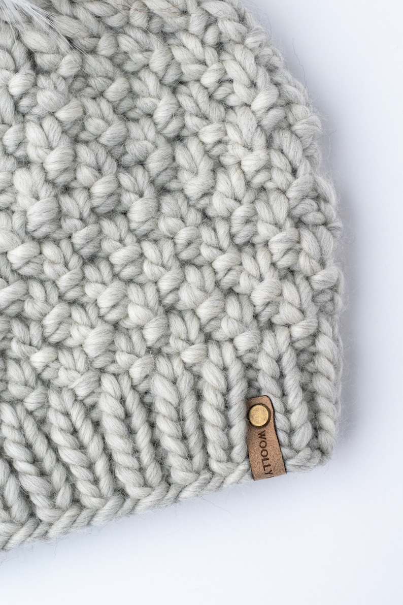 May include: A gray knitted beanie with a brown leather tag that says "WOOLLEY".