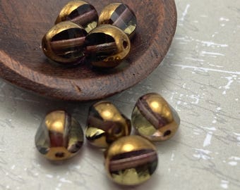 Black diamond Czech glass tricon cut beads displayed on a wooden bowl and white textured surface, showing bronze detailing.