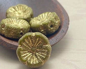 Four peridot green gold etched Czech glass hibiscus flower beads in a wooden bowl on a plain background.