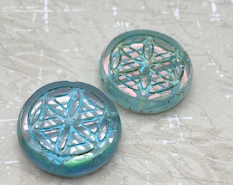 Two turquoise blue Czech glass flower of life beads with gold wash on a plain textured background.