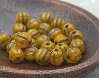 Twenty-five golden yellow Czech glass melon beads with dark striped detail on a wooden dish.