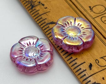 Two rose pink Czech glass flower beads with iridescent AB finish and dark stamen detail, shown next to a wooden ruler.