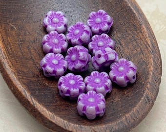 Twelve lilac Czech glass flower beads with purple wash arranged in a wooden dish against a pale background.