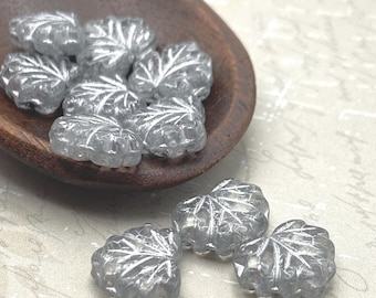Silver grey Czech glass maple leaf beads with detailed veining shown in a wooden bowl and on a pale background.