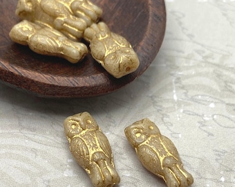 Six cream Czech glass owl beads with gold lustre finish displayed in and beside a dark wooden dish on a light fabric.