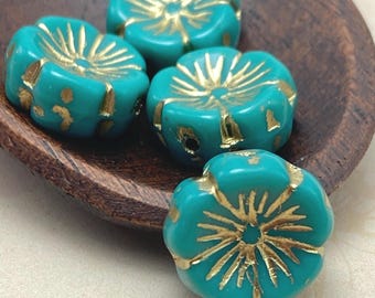 Four teal Czech glass hibiscus flower beads with gold wash detail on a wooden bowl.