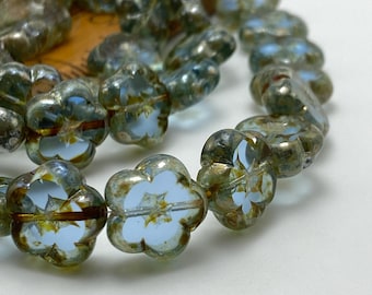Czech glass flower beads in clear aqua blue with Picasso finish strung on wooden bead board, showing roughly thirty beads.