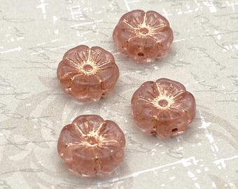 Four peachy pink hibiscus Czech glass beads with copper wash shown on a cream background.
