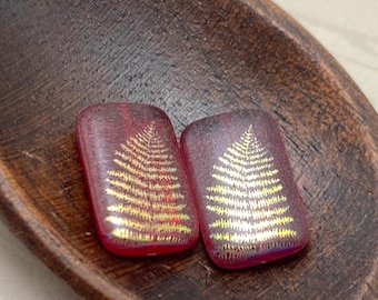 Two matte red rectangle Czech glass beads with gold laser-etched fern design, shown in a wooden bowl.