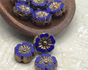 Eight deep blue Czech glass hibiscus flower beads with gold wash detail displayed on a wooden dish and white linen cloth.