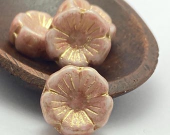 Three Czech glass hibiscus flower beads in powder pink with gold lustre detail displayed in a small brown metal dish.