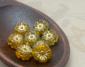 Eight yellow Czech glass Hawaiian hibiscus flower beads with gold wash in a wooden dish against a pale background.