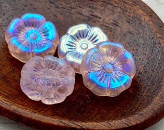 Four Czech glass hibiscus flower beads with pale pink and iridescent blue finishes displayed on a wooden dish.