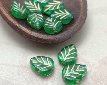 Ten Czech mint leaf beads in clear emerald green with gold wash, shown on a wooden dish and pale background.