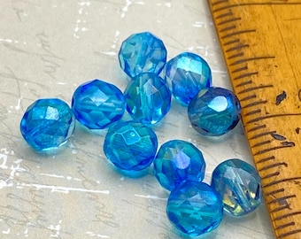 Nine faceted round Czech glass beads in bright blue with AB iridescent coating, next to a wooden ruler for scale.